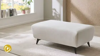 Hocker steht presentabel auf Teppich, natürliches Licht vom Fenster erhellt die Szene